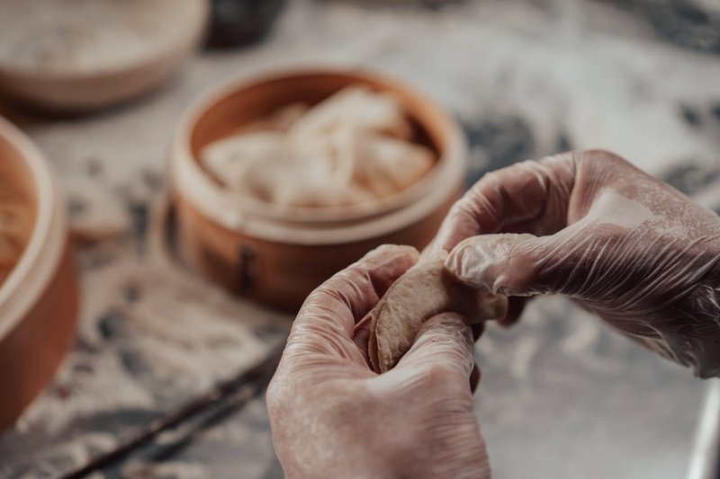 Close-up of hands folding homemade Asian dumplings on a floured surface