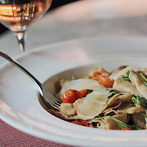Glasses of wine and plates of pasta set out on a long table for a tasting